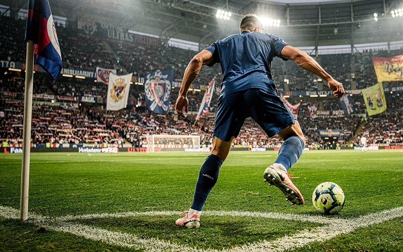 Jugador de fútbol ejecutando saque de esquina en estadio con afición al fondo