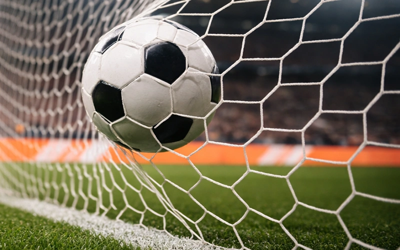 Portería de fútbol con red y balón entrando durante partido nocturno